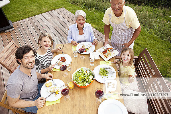 Grandfather serving food from barbecue grill for family at garden table
