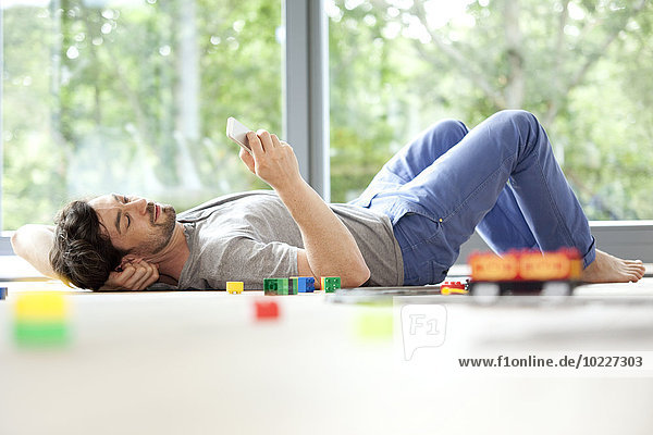 Mann auf dem Boden liegend mit Handy neben Spielzeugeisenbahn