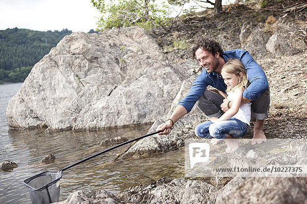 Vater und Tochter mit Tauchnetz am Seeufer