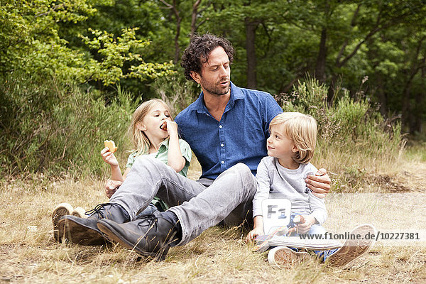 Vater mit zwei Kindern beim Picknick am Waldrand