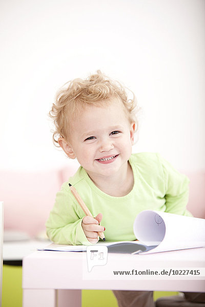 Porträt des grinsenden kleinen blonden Mädchens mit Buntstift