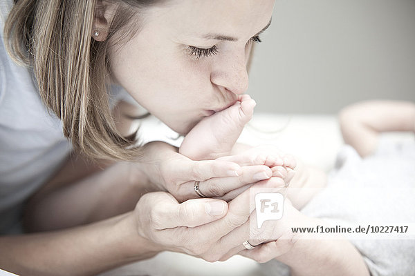 Young mother kissing foot of baby girl
