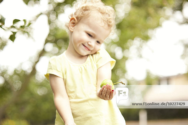 Kleines Mädchen im Garten stehend mit Apfel in der Hand