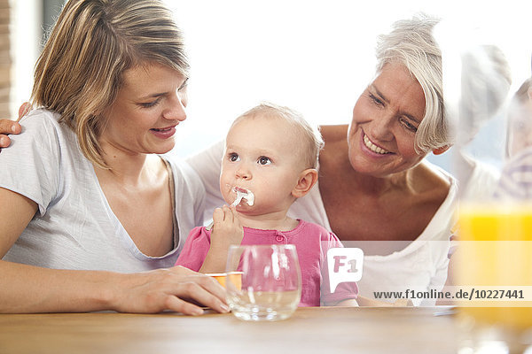 Großmutter und Mutter sehen sich das Mädchen an  das Joghurt isst.