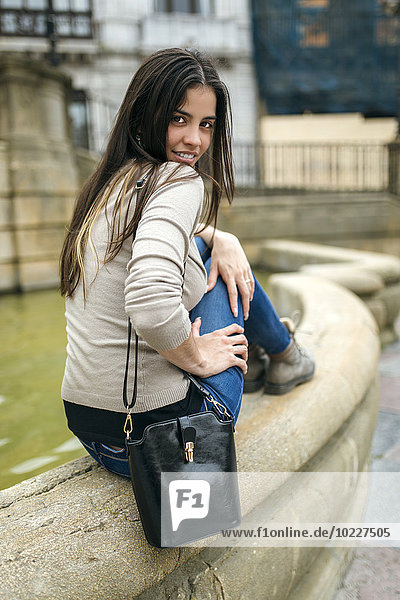 Spanien  Oviedo  junge Frau sitzt am Rande eines Brunnens in der Altstadt