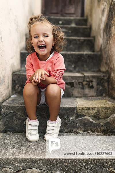 Porträt eines lachenden kleinen Mädchens auf einer Treppe sitzend