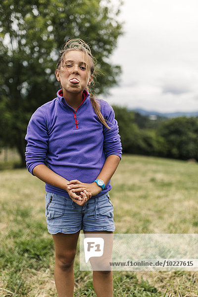 Portrait of girl standing on a meadow sticking out tongue