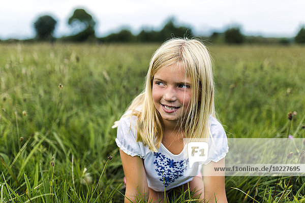 Porträt eines Mädchens  das auf einer Wiese kniend etwas beobachtet.