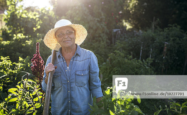 Porträt der lächelnden Seniorin mit Strohhut im Garten