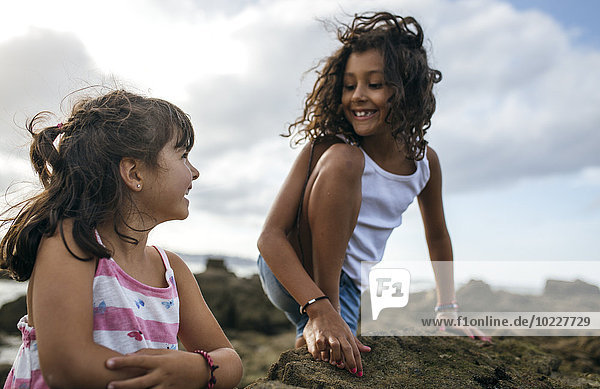 Spain  Gijon  portrait of two smiling little girls playing at rocky coast