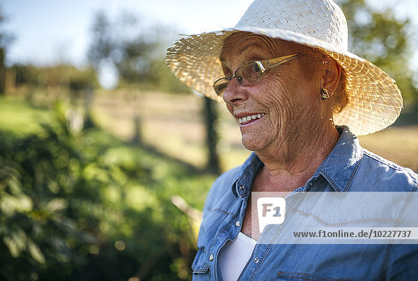 Porträt der lächelnden Seniorin mit Strohhut im Garten