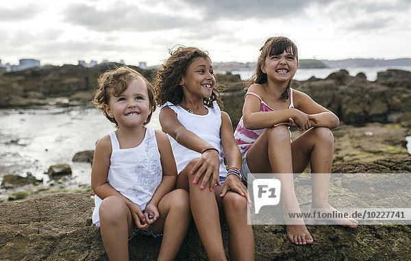 Spain  Gijon  group picture of three little girls sitting at rocky coast