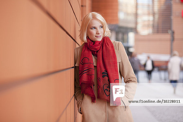 Portrait of young woman with red scarf leaning on wall