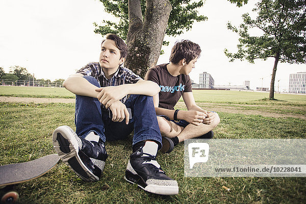 Germany  Berlin  two teenage boys in bad mood sitting under a tree