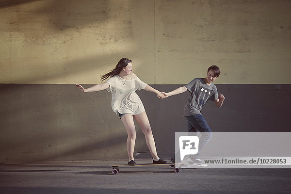 Teenager-Junge zieht seine Freundin auf einem Longboard.