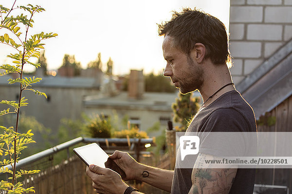 Deutschland  Berlin  Erwachsener Mann auf der Dachterrasse mit digitalem Tablett