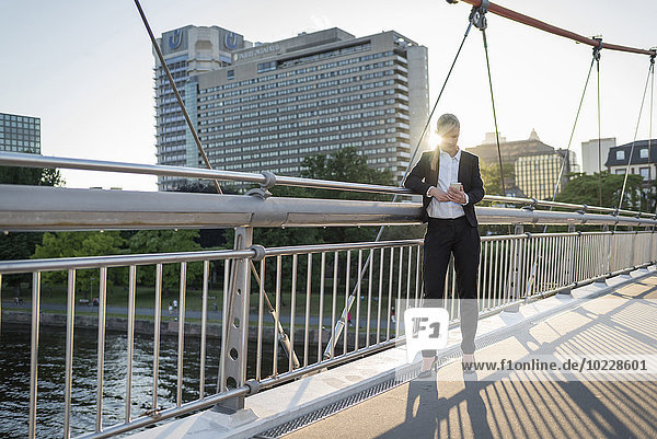 Geschäftsfrau steht in der Dämmerung auf einer Brücke mit dem Smartphone