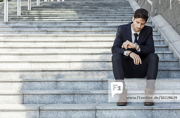 Porträt eines jungen Geschäftsmannes  der auf einer Treppe sitzt und die Zeit überprüft.