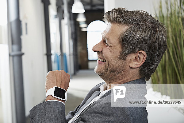 Lächelnder Geschäftsmann im Büro mit smartwatch