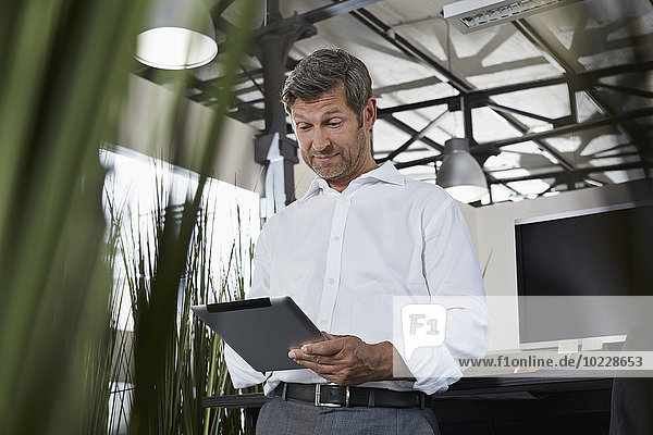 Überraschter Geschäftsmann im Büro mit Blick auf digitales Tablett