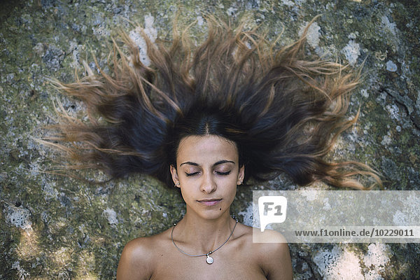 Portrait of young woman lying on a rock with tousled hair and closed eyes
