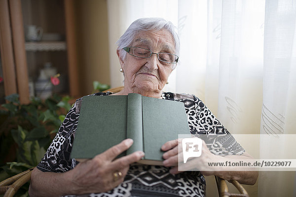 Seniorin bei einem Nickerchen mit Buch in der Hand zu Hause