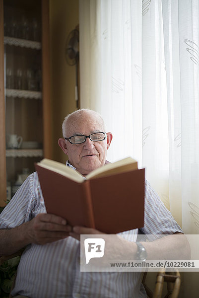 Ein älterer Mann  der zu Hause ein Buch liest.