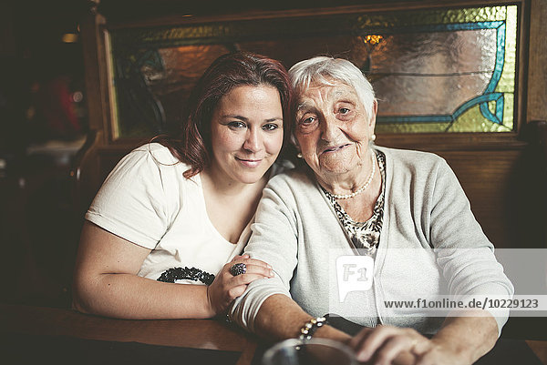 Porträt einer lächelnden Seniorin und ihrer Enkelin  die Kopf an Kopf in einem Restaurant sitzen.