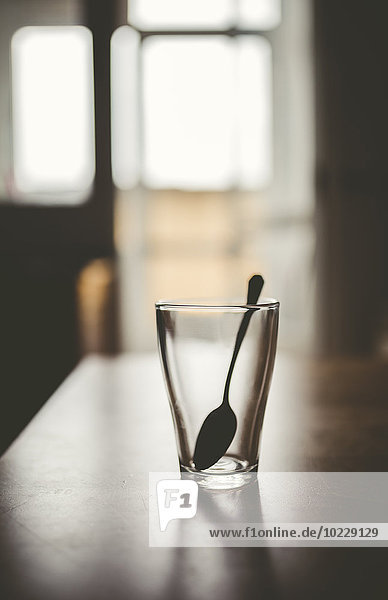 Leeres Glas mit Teelöffel auf einem Tisch bei Gegenlicht