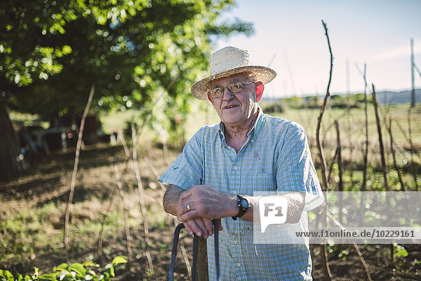 Portrait of smiling farmer wearing straw leaning on hachet
