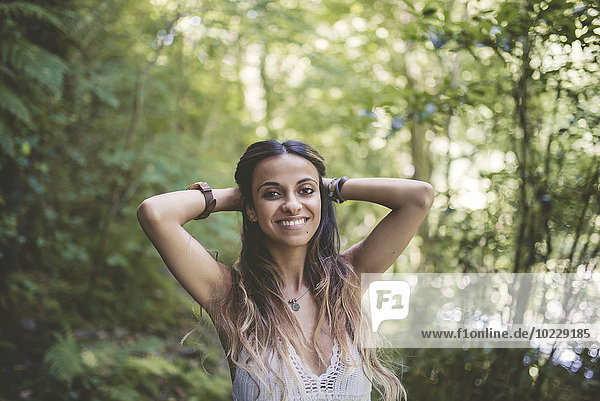 Porträt einer glücklichen jungen Frau im Wald mit den Händen hinter dem Kopf