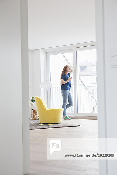 Young woman standing in her living room looking through window