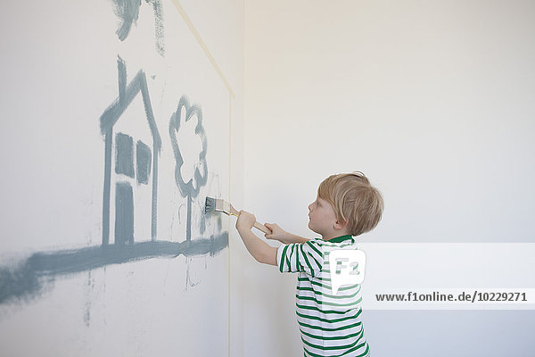 Kleiner Junge malt Haus und Baum an der Wand seines neuen Zimmers