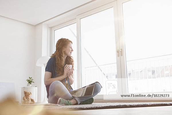 Young woman sitting on the floor of her living room looking through window