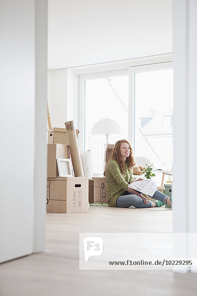 Junge Frau in neuer Wohnung mit Kartons im Grundriss