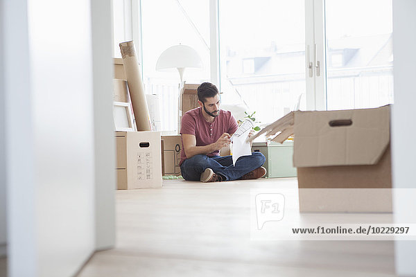 Young man in new flat with cardboard boxes holding ground plan