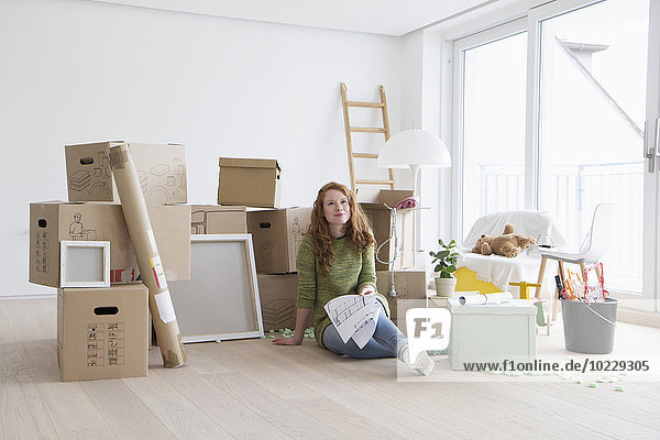 Junge Frau in neuer Wohnung mit Kartonschachteln mit Grundriss