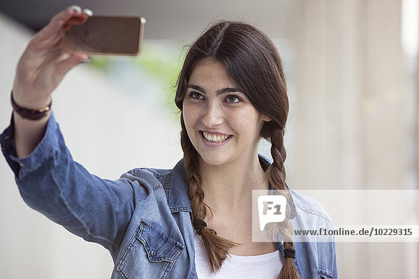 Junge Frau mit Zöpfen nimmt einen Selfie mit Smartphone
