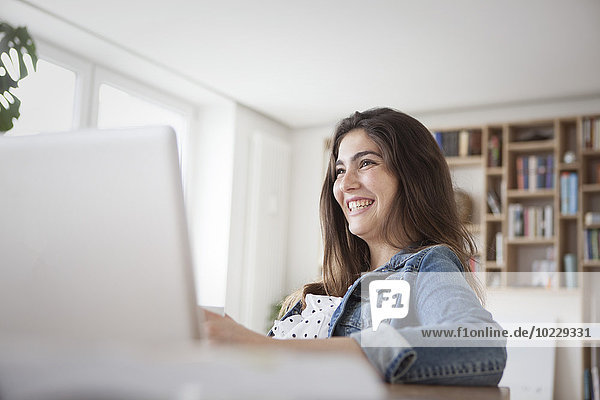 Lächelnde junge Frau mit Laptop zu Hause