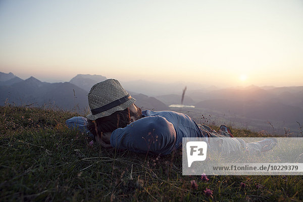 Österreich  Tirol  Unterberghorn  Mann entspannt sich bei Sonnenuntergang auf Almen