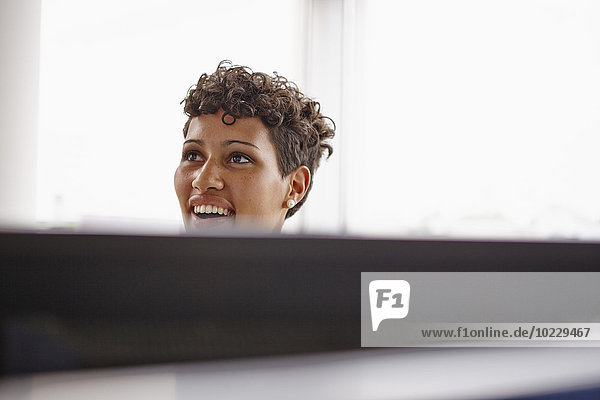 Lächelnde junge Frau im Büro hinter dem Computerbildschirm