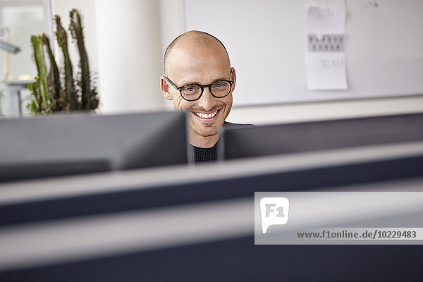 Lächelnder Mann im Büro hinter Computerbildschirmen