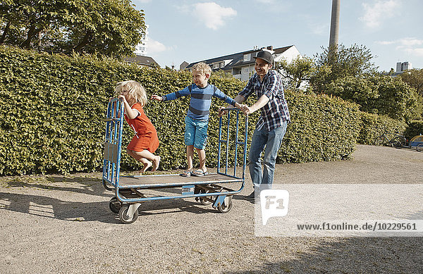 Vater Schiebewagen mit zwei Kindern im Kleingartenbereich