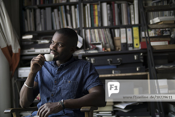 Junger Mann trinkt Kaffee in seinem Atelier