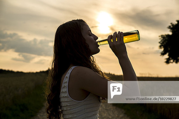 Junge Frau trinkt aus Glasflasche,  Abendsonne