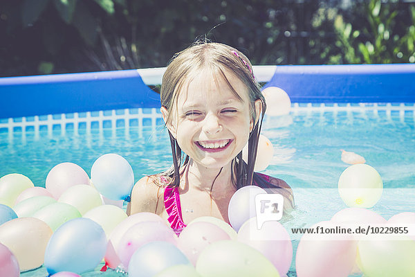 Glückliches Mädchen im Schwimmbad umgeben von Luftballons