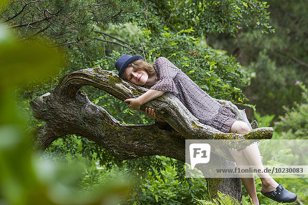 Glückliche junge Frau auf einem Baumstamm liegend