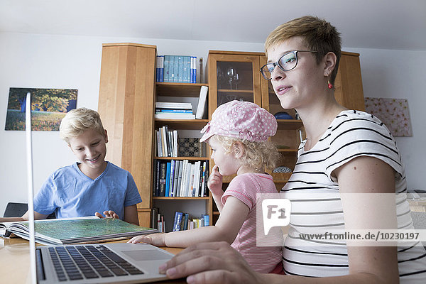Schwangere Frau mit Sohn und kleiner Tochter zu Hause mit Laptop