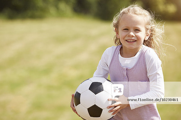 Portrait of smiling little girl with soccer ball on a meadow