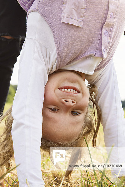 Portrait of happy little girl doing handstand on a meadow